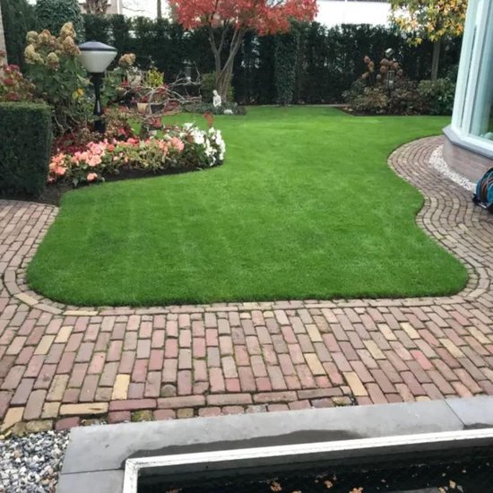 Een prachtig aangelegde, groene gazon met een border van bloemen en struiken en een bakstenen pad.