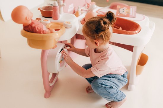 Meisje met rood haar speelt met roze poppenverzorger. Ze opent het luikje van de magnetron.