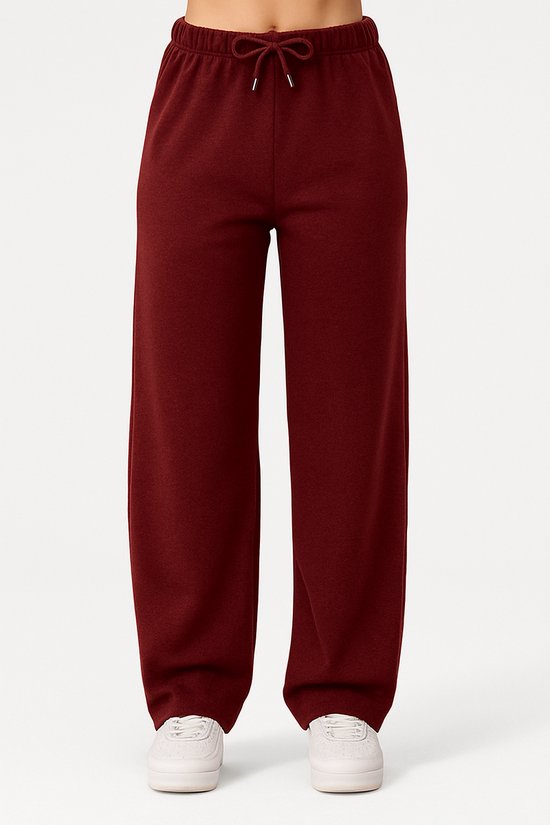 Vooraanzicht van een bordeauxrode joggingbroek met wijde pijpen en trekkoord. Witte sneakers.