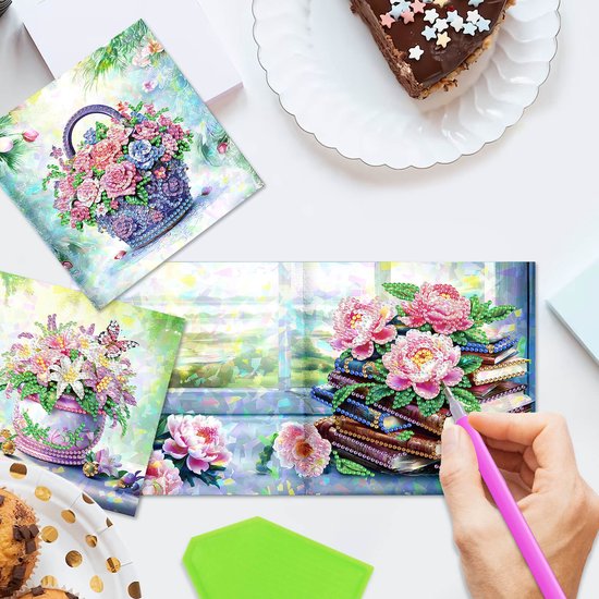 Diamond painting kaarten met bloemstukken in manden en opgestapelde boeken.