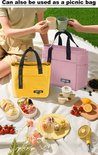 Roze en gele lunchtas op een picknickkleed met eten, vers fruit en drinken, met mensen op de achtergrond.