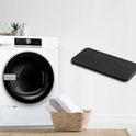 Zwart rechthoekig schuimfilter met twee gaten, gepresenteerd naast een wasmachine en een mand met handdoeken.
