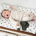 Baby ligt op een wit verschoonkussen met groen bloemenprintje. Draagt een beige longsleeve romper.