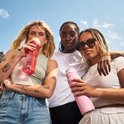 Trois jeunes femmes avec des gourdes Kambukka. L'une tient une gourde rose avec une paille, l'autre une gourde rose texturée.
