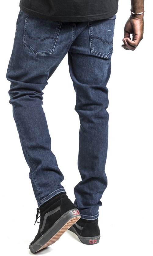 De achterkant van een man in een donkerblauwe jeans, met zwarte hoge Vans schoenen.