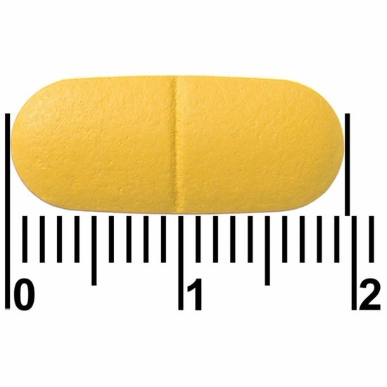 Een enkele gele Davitamon tablet met een deelstreep, gemeten met een liniaal.