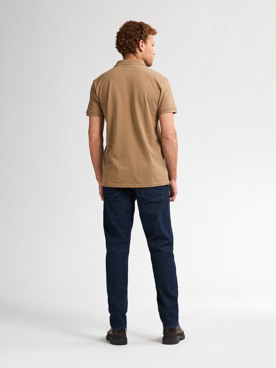 Man met krullend haar, achterkant, draagt een bruine polo en donkerblauwe jeans.