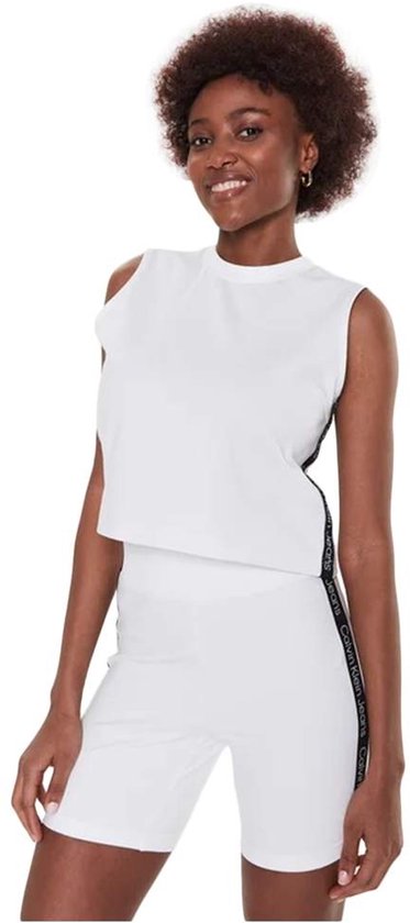 Model in wit mouwloos T-shirt met Calvin Klein logo tape op de zijkant, gecombineerd met witte fietsbroek.