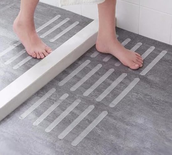 Voeten op grijze douchebodem met doorzichtige antislipstrips in parallelle lijnen.