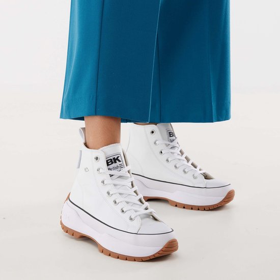 Voeten in witte hoge sneakers met bruine rubberen zolen, gedragen met een blauwe broek.