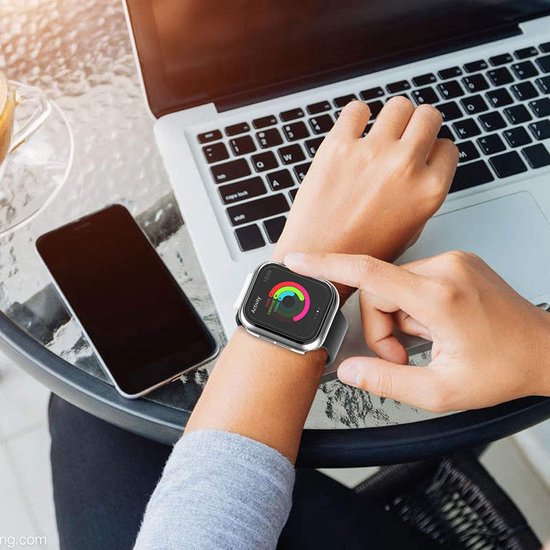 Persoon draagt Apple Watch met transparante hoes aan pols, naast laptop.