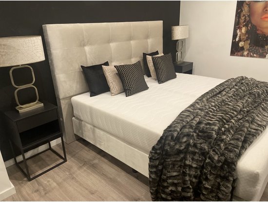 Chique slaapkamer met beige boxspring, vier kussens, sprei, nachtkastje met lamp en schilderij aan de muur.