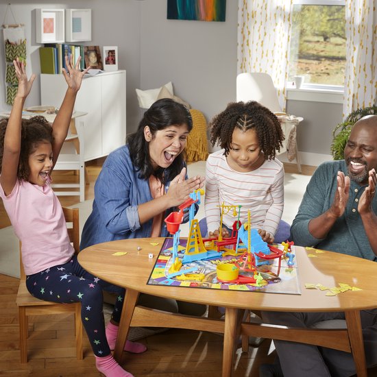 Een gezin viert een succes in het spel "Muizenval" aan een houten tafel.
