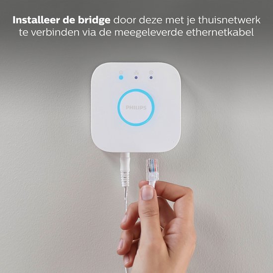 Witte Philips Hue Bridge wordt met een ethernetkabel aangesloten op een muur.
