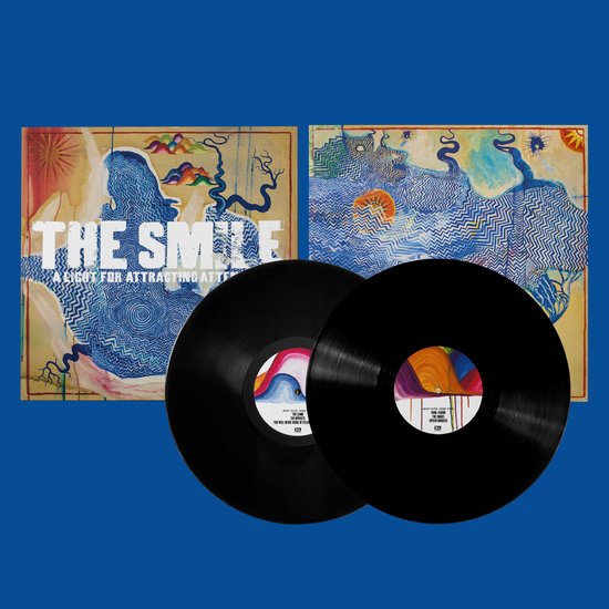 Twee zwarte vinylplaten met kleurrijke labels, naast een albumhoes met blauwe, abstracte patronen en de tekst 'THE SMILE A LIGHT FOR ATTRACTING ATTENTION'.