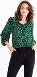Model met zwarte broek met strikceintuur en groen hartjesblouse met ruchekraag.