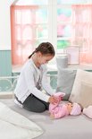 Meisje op bed kleedt baby pop in roze pyjama aan. Baby Annabell.