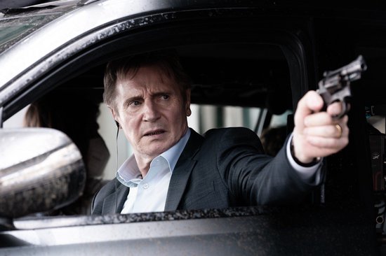 Een man in een pak met een pistool in zijn hand, kijkend uit een autoportier.