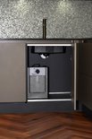 Compacte boiler met grijze behuizing onder een keukenaanrecht met mozaïek achterwand en gouden kraan.