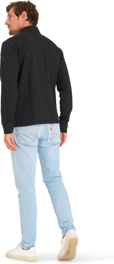 Man draagt zwarte trui met ritskraag, lichtblauwe jeans en witte sneakers, achterkant zichtbaar