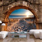 Fotobehangkoning - Behang - Vliesbehang - Fotobehang Uitzicht op het Strand door de Stenen Boog - Arch and Beach - 200 x 140 cm