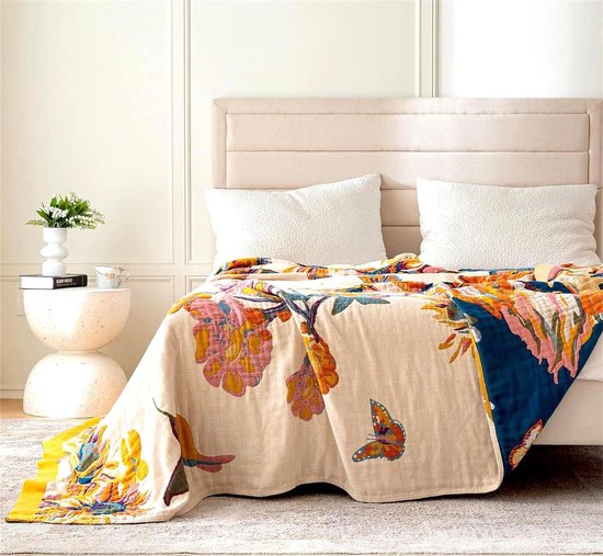 Dubbelzijdige deken met bloemen- en vlinderprint, op een bed met witte kussens.
