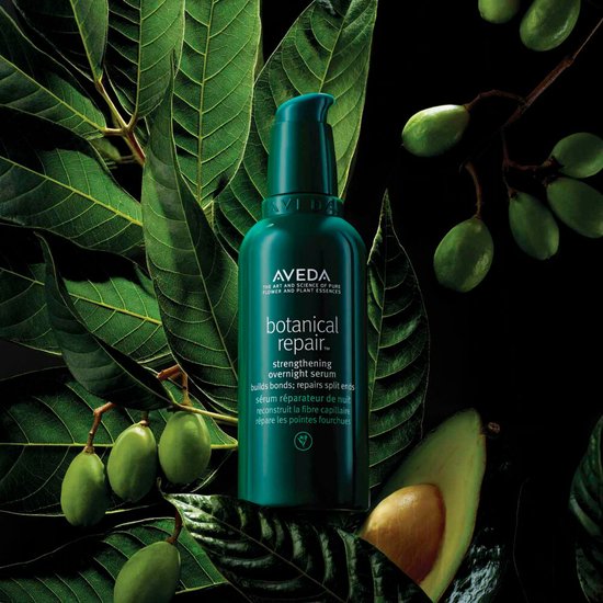 Aveda Botanical Repair verzorgende nachtserum omringd door groene bladeren en avocado's.