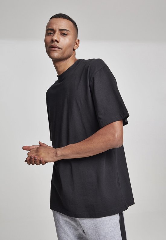 Man in zwart oversized T-shirt en grijze joggingbroek met zwarte streep, handen bij elkaar.