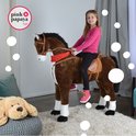 Meisje in roze shirt zittend op een groot bruin pluche paard met zadel en rode bandana in een kinderkamer.