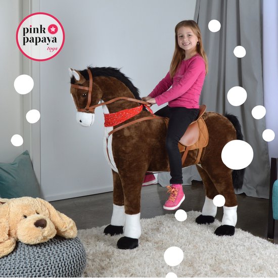 Meisje in roze shirt zittend op een groot bruin pluche paard met zadel en rode bandana in een kinderkamer.