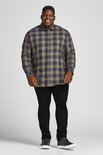 Man met geruite blouse en zwarte jeans, staand.