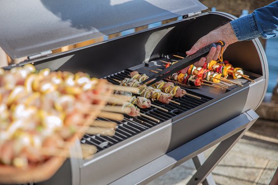 Hand gebruikt zwarte Boretti tang om spiesjes in een grill te draaien.