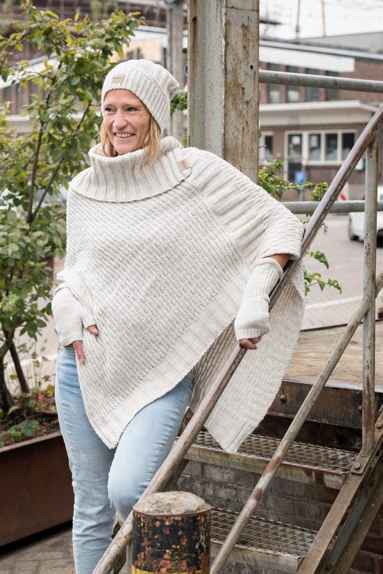 Model in crème gebreide poncho met hoge kraag en vingerloze handschoenen. Draagt een lichte spijkerbroek.