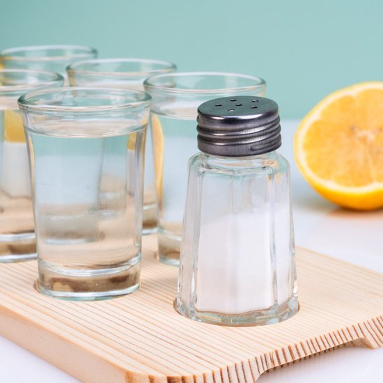 Verres à shot avec salière et quartiers de citron sur planche en bois.