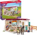 De Schleich Horse Club Zadelkamer speelset toont een speelgoedpaard en -ruiter voor een gebouw met zadels en hoofdstellen aan de muur.