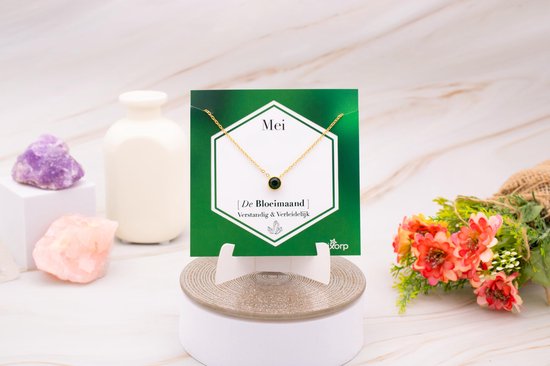 Gouden ketting met smaragdgroene hanger op kaartje, tentoongesteld op een display.