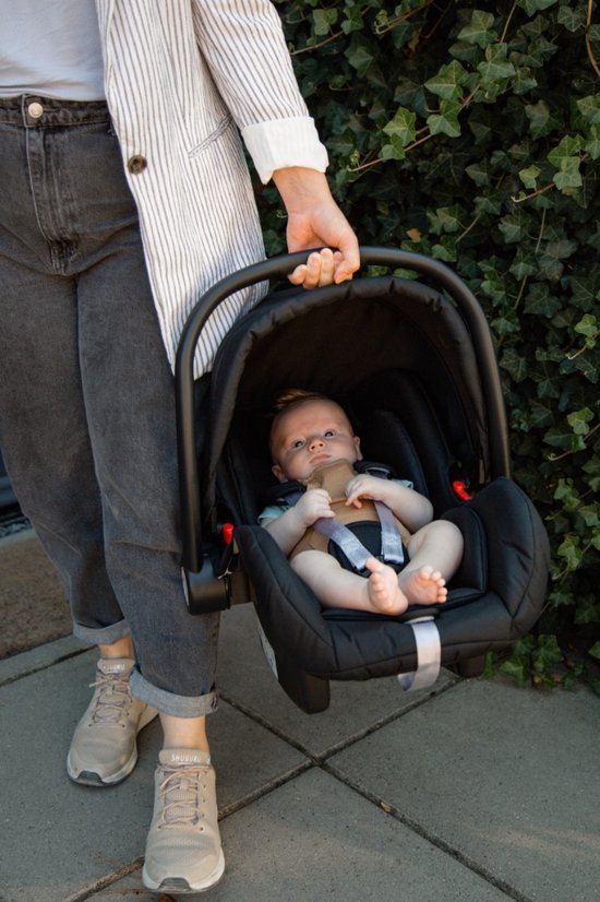 Een baby in een zwarte autostoel gedragen door een persoon.