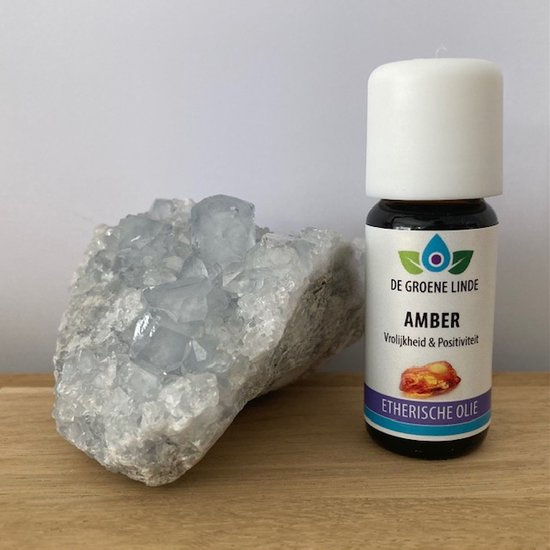Flesje amber etherische olie van De Groene Linde, met etiket met 'Amber Vrolijkheid & Positiviteit'. Naast een helderblauwe kristal.