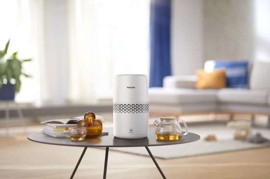 Une femme lit dans un fauteuil suspendu dans un salon lumineux, avec un humidificateur d'air blanc sur une table d'appoint.