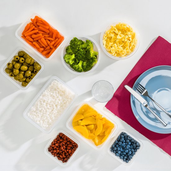 Gekookte groenten en fruit in STOSH vershouddozen op een witte tafel met een blauw bord.
