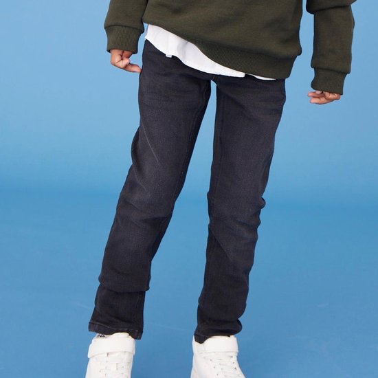 Jongens model in donkergrijze slim fit jeans en witte sneakers.