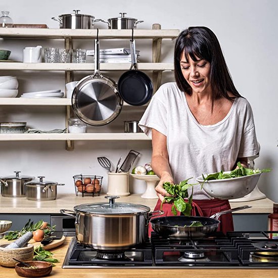 Vrouw met witte T-shirt kookt op gasfornuis met verschillende pannen en ingrediënten.