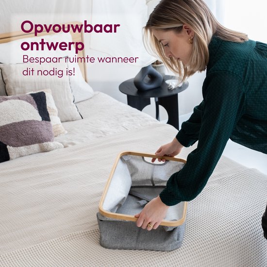 Vrouw die een grijze wasmand met bamboe rand opvouwt op een bed.