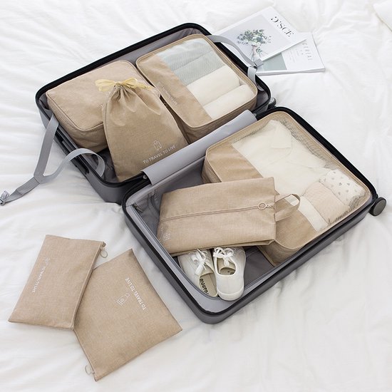 Beige reishoesjes en organisatorzakken in een koffer met kleding en witte schoenen.