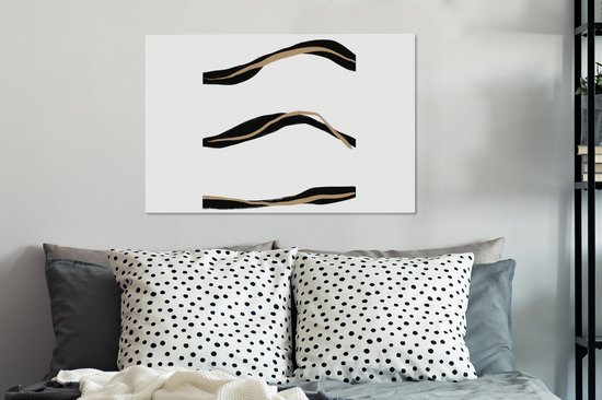 Abstract schilderij met drie zwarte en goudkleurige lijnen boven een bed met gestreepte kussens.