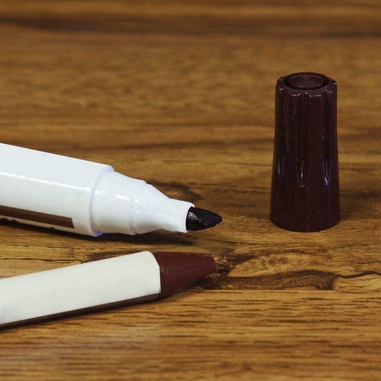 Een witte marker met bruine dop naast een bruin krijtje op een houten ondergrond.