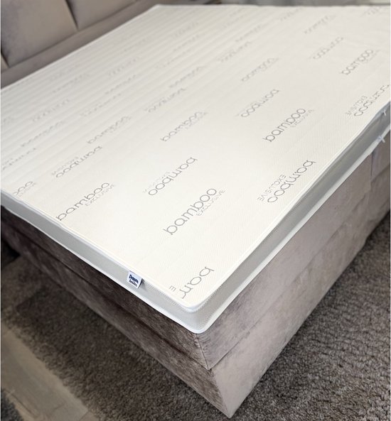 Witte matras met 'bamboo exclusive' opdruk op taupe bedbodem met grijs vloerkleed.