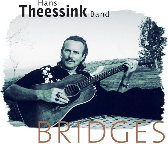 Hans Theessink Band 'Bridges'. Un homme avec une moustache joue de la guitare acoustique, assis sur une couverture à l'extérieur.