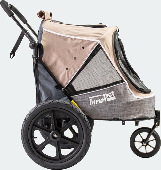 Beige hondenbuggy met grijze stof, grote achterwielen en een zwenkwiel aan de voorkant. Zijaanzicht.