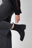 Model draagt zwarte leren Chelsea boots met grijze jeans met rafels.